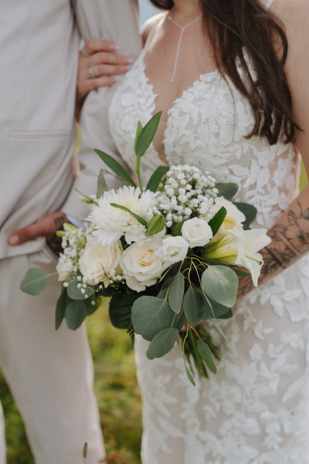 Close up of Ashley's white bouquet and lace dress beside Kenneth