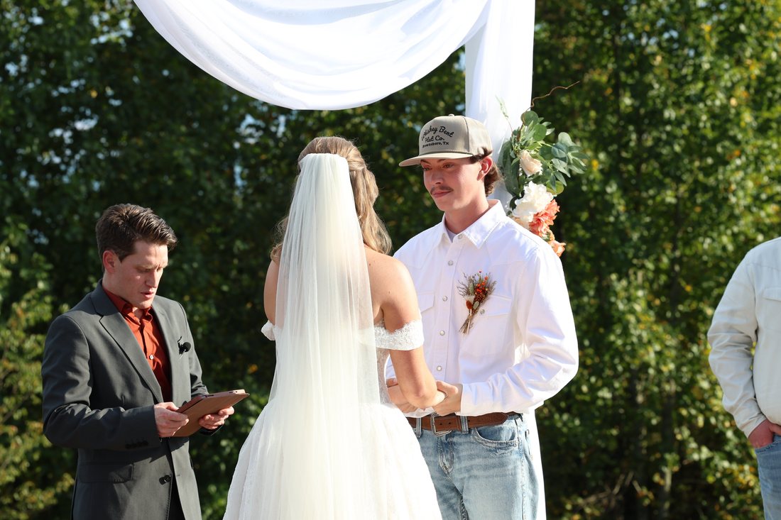 Matthew holding Autumn's hands during their vows, her veil down her back