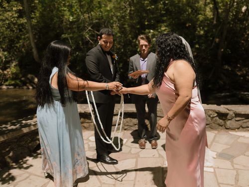 Two women presenting the white wedding lasso to Raynita and Charlie at the altar